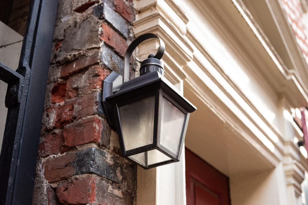 A porch light during the day in front of a red brick wall.