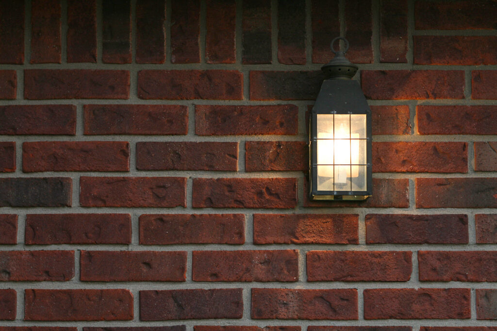 A porch light in front of a red brick wall.